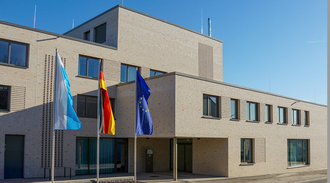 modernes Gebäude mit Flachdach, davor drei Flaggen